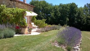 A stone building with a garden, a lawn, and a row of lavender plants.