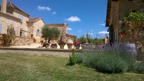 A stone building with a tiled roof, a grassy lawn, and potted plants.