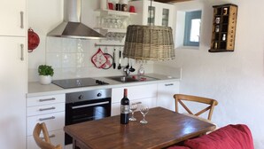 A kitchen with white cabinets, a stainless steel stove, a hanging wicker lamp, and a dining table with a red cushion.