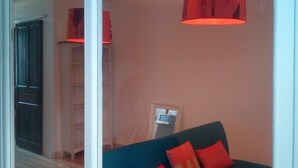 Quarto com sofá azul escuro, almofadas vermelhas e luminária pendente vermelha.