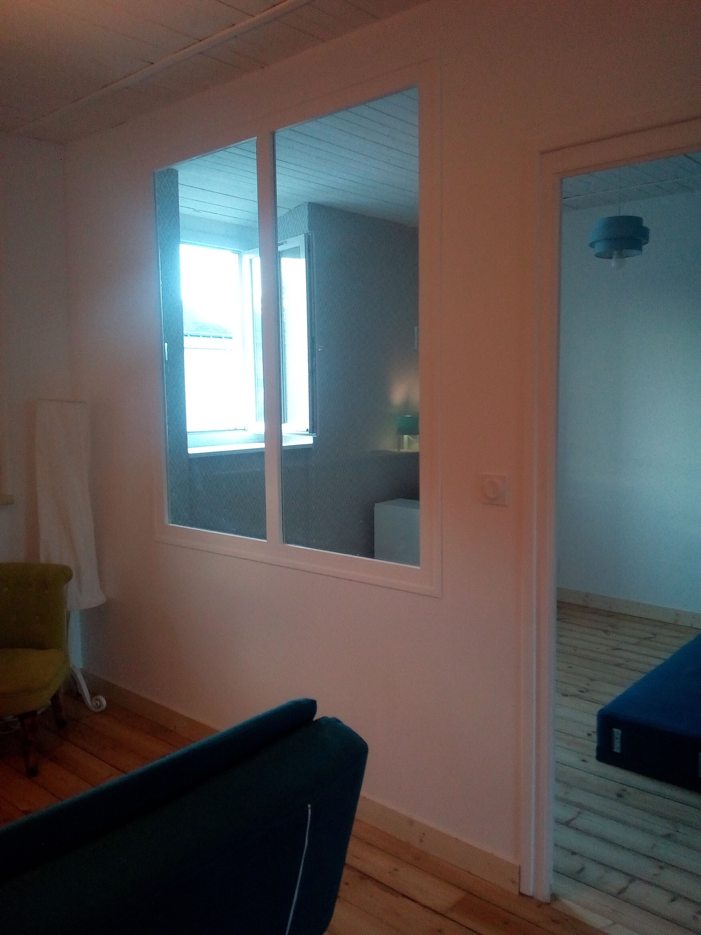 A room with a large window, a chair, a small table, and a door leading to another room.