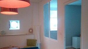 Quarto com sofá azul, uma pequena janela e porta que dá para outro cômodo.
