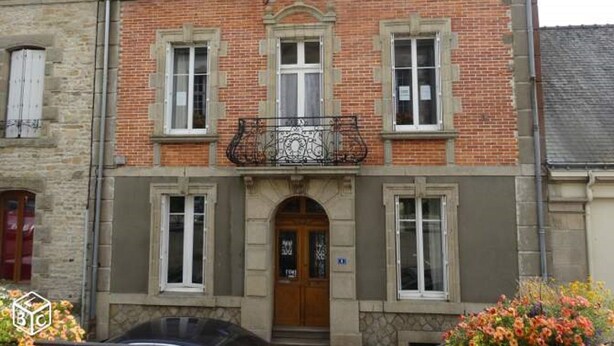 Um edifício de dois andares com fachada de tijolos, janelas emolduradas por branco e uma porta de madeira.
