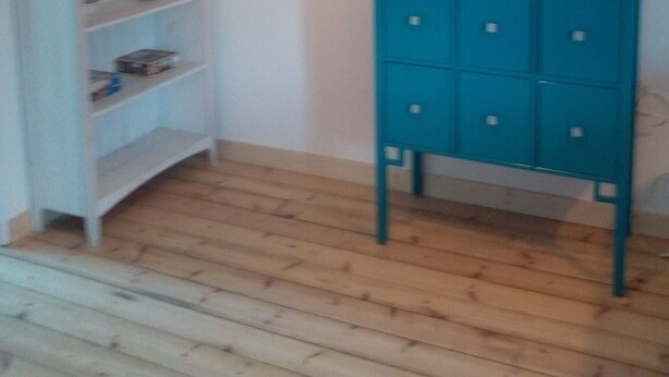 A room with a wooden floor, a teal cabinet with drawers, and a white shelf unit with various items.