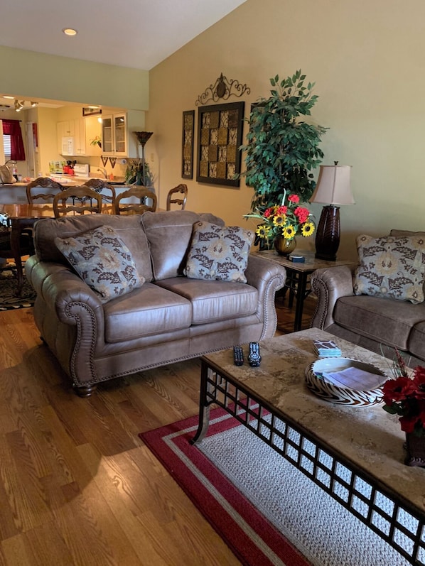 A living room with a brown leather sofa, a coffee table, and a dining area with wooden chairs and a table.