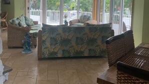 A spacious living area with a large sofa, two chairs, a dining table, and a ceiling fan.