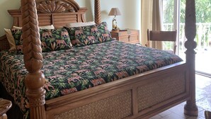 A four-poster bed with a floral bedspread, a wooden headboard, and a large mirror above it.