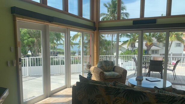 A spacious room with a large sliding glass door leading to a balcony. Inside, there is a wicker sofa and a small round table.