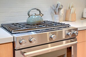 Une cuisine en acier inoxydable équipée d’une cuisinière à gaz, d’un four et d’une bouilloire posée sur le plan de travail.