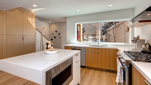 A modern kitchen with wooden cabinets, a white countertop, a built-in oven, and a window with a view of a snowy landscape. - Scandinavian 72 Vantage Condo with Private Hot Tub by RedAwning (Park City)