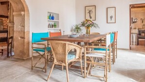 A dining area with a wooden table and wicker chairs, a vase with flowers, and a shelf with bottles. - Typical country property with Yacuzzi pool and large outdoor area (Porreres)