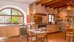 A rustic kitchen with wooden cabinets, a stone wall, and a large window. - Typical country property with Yacuzzi pool and large outdoor area (Porreres)