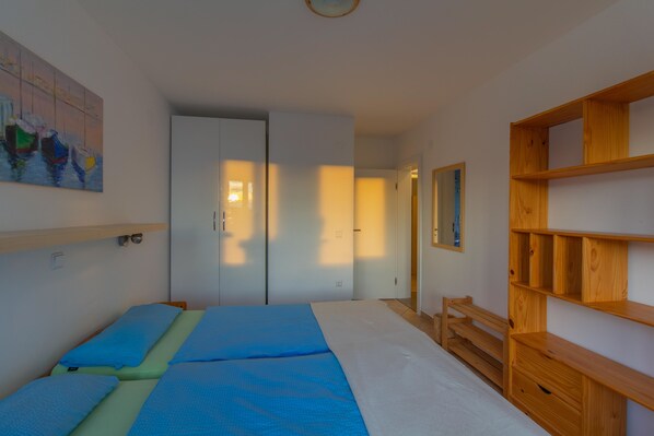 A bedroom with two beds, a wardrobe, a wooden shelf unit, and a painting on the wall.
