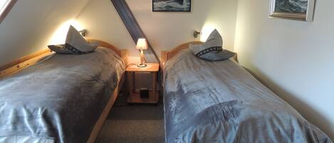 A small, cozy room with two single beds, a nightstand with a lamp, and a painting of a sailboat on the wall.