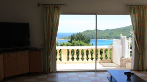 A room with a TV, a table, and a view of the sea. - Superb infinity pool villa with stunning sea views in Favone  (Sari-Solenzara)