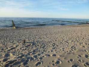 Ein Sandstrand mit Fußabdrücken und einer Holzkonstruktion, die ins Wasser hineinragt.