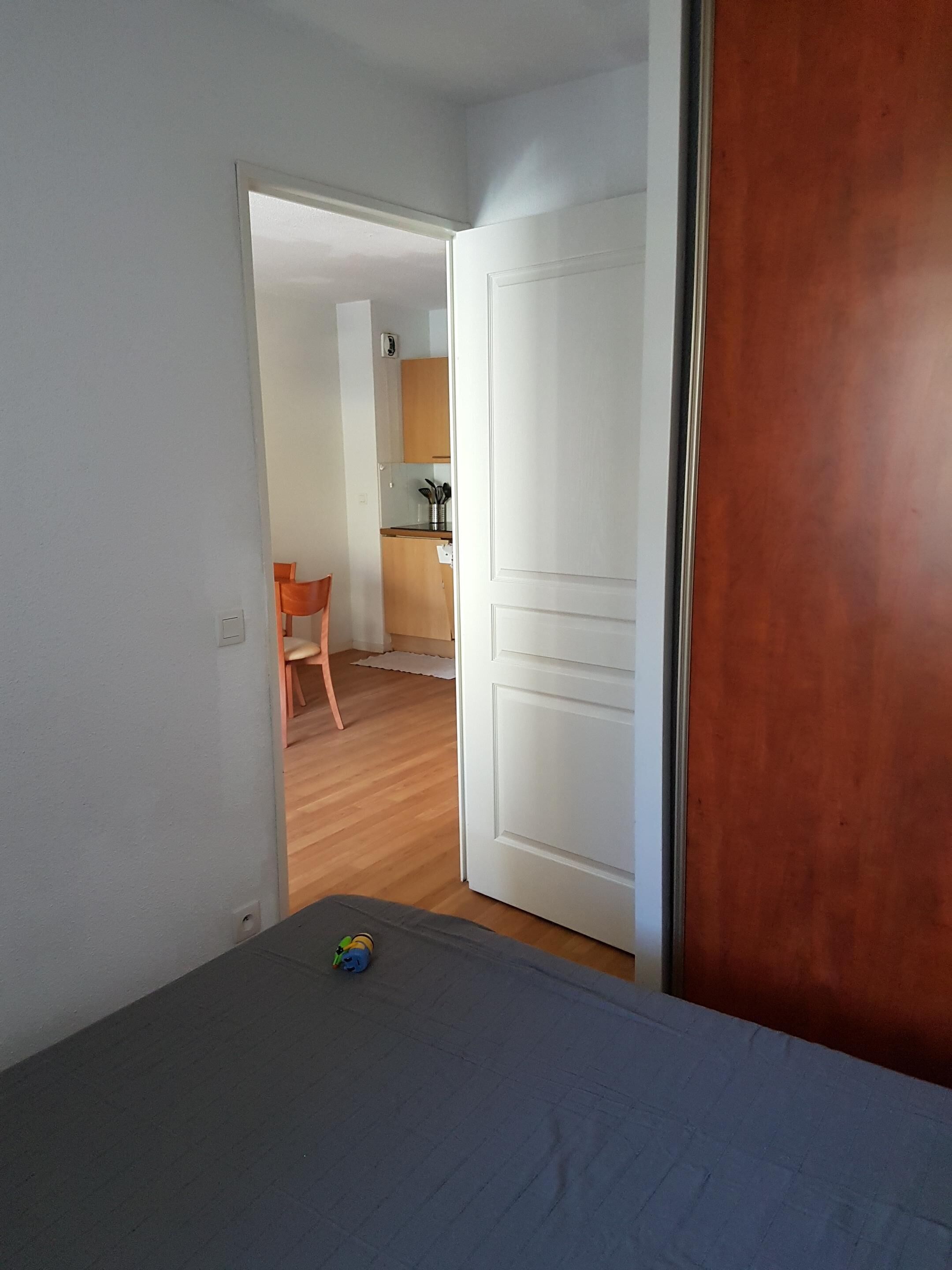 Una habitación con una cama, una puerta de madera y vistas a una zona de cocina con una silla y una encimera.