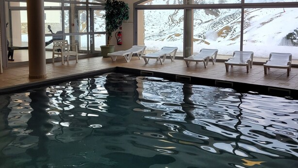 An indoor swimming pool with clear glass walls, a fire extinguisher, and lounge chairs. - La Mongie 2 rooms 4 persons Residence Pic du Midi parking and swimming pool (Bagnères-De-Bigorre)