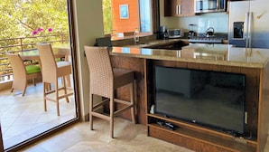 Una cocina moderna con armarios de madera, un televisor grande y un comedor con sillas de mimbre.