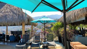 Una terraza con sombrillas de paja, sillones de descanso y vista a la ciudad.