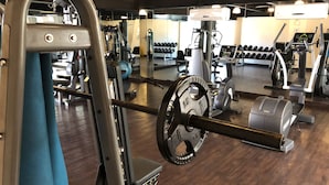 Un gimnasio con diverso equipo de ejercicio, incluyendo una jaula de sentadillas, mancuernas y una cinta de correr.