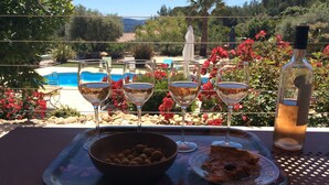 Una mesa con cuatro copas de vino, un cuenco de aceitunas, un plato con un pastel y una botella de aceite de oliva.