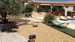 Un edificio de estilo mediterráneo con piscina, zona de estar al aire libre y jardín con rocas y plantas.
