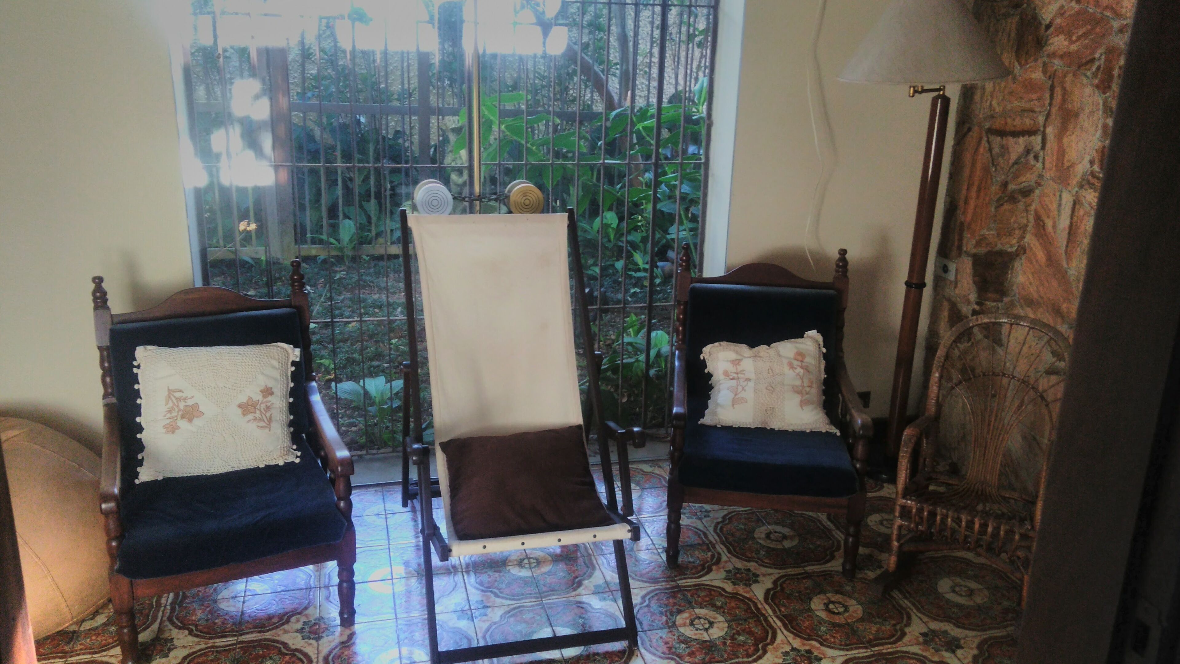 A room with two wooden chairs with cushioned seats and backs, a patterned floor, and a view through a window to a garden.
