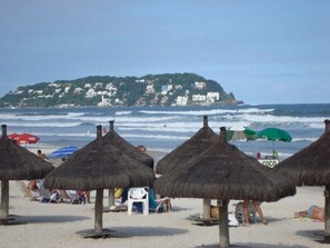 A beach with thatched umbrellas and a view of a hillside with buildings.