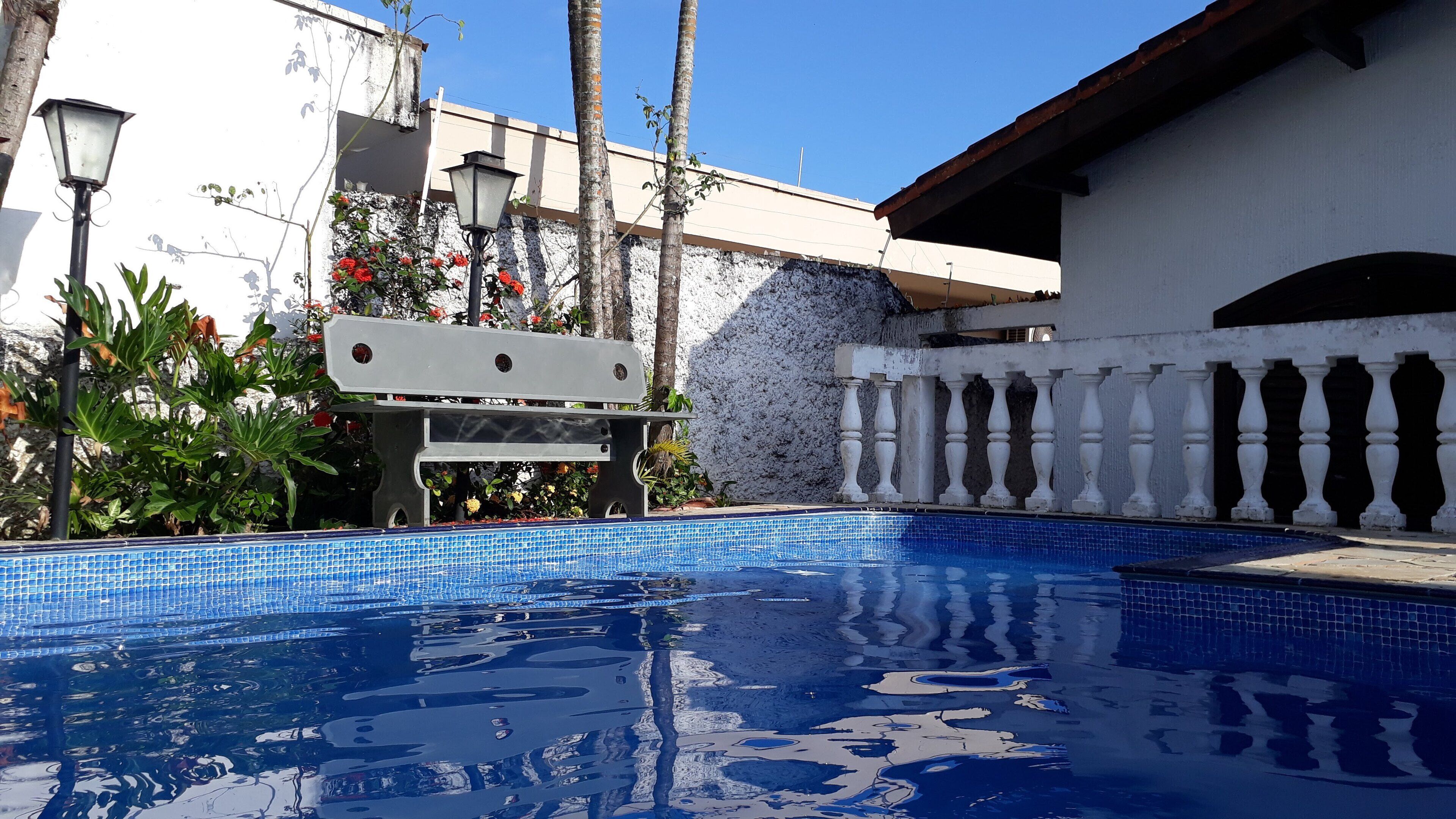 A swimming pool with blue tiles, surrounded by a white building with a balcony and a railing.