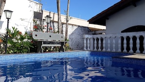 Una piscina con azulejos azules, rodeada por un edificio blanco con balcón y barandilla.