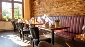 Interior de restaurante con paneles de madera, una zona de asientos con un largo banco y una fila de mesas con sillas.