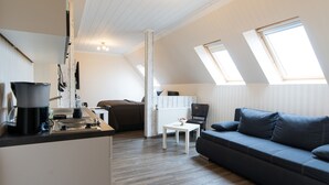 Un espacio habitable compacto con kitchenette, sofá, mesa de comedor y silla. Cuenta con tragaluces que proporcionan luz natural.