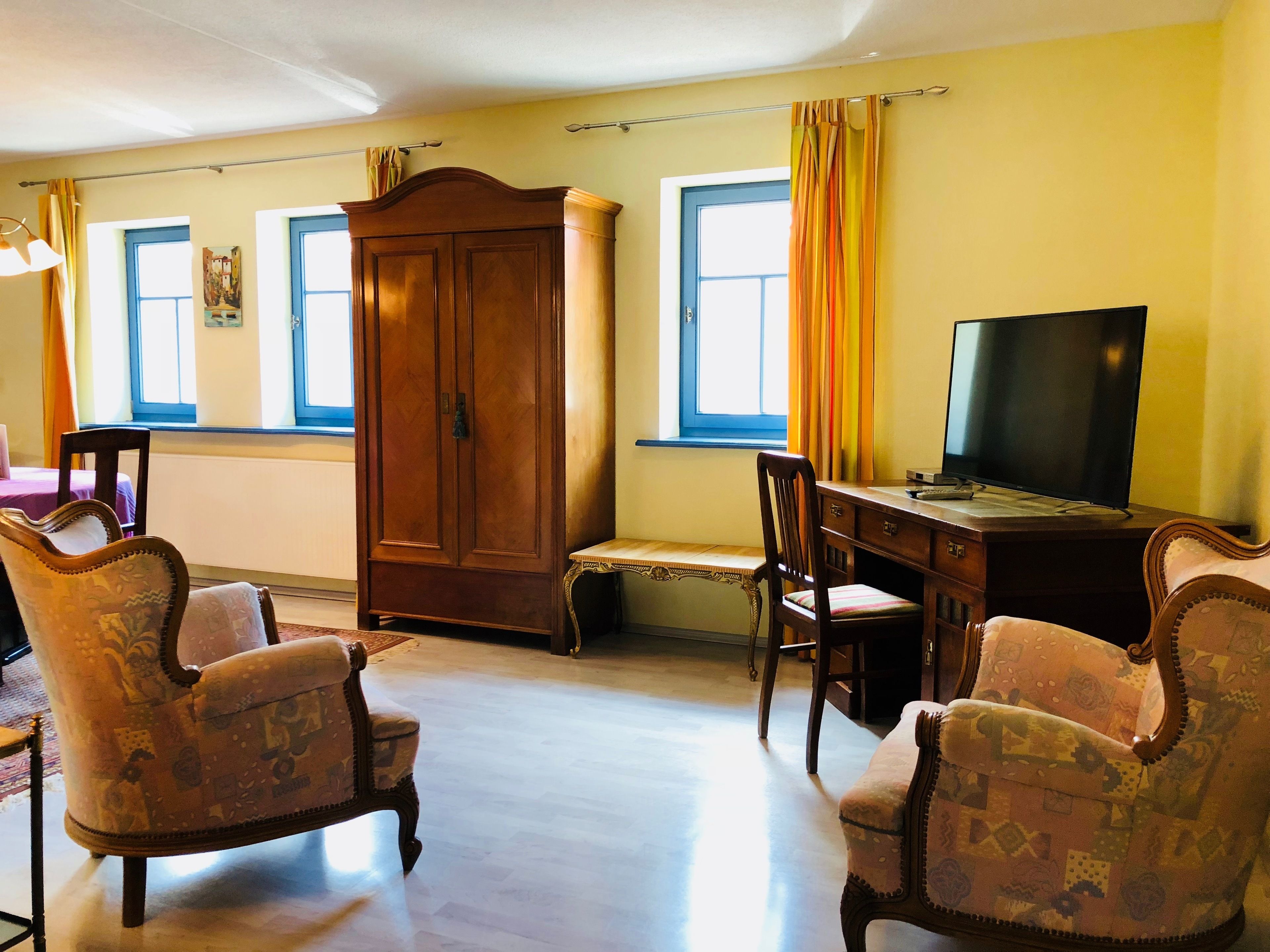 Una habitación con un armario de madera, un escritorio con televisor y sillones estampados.