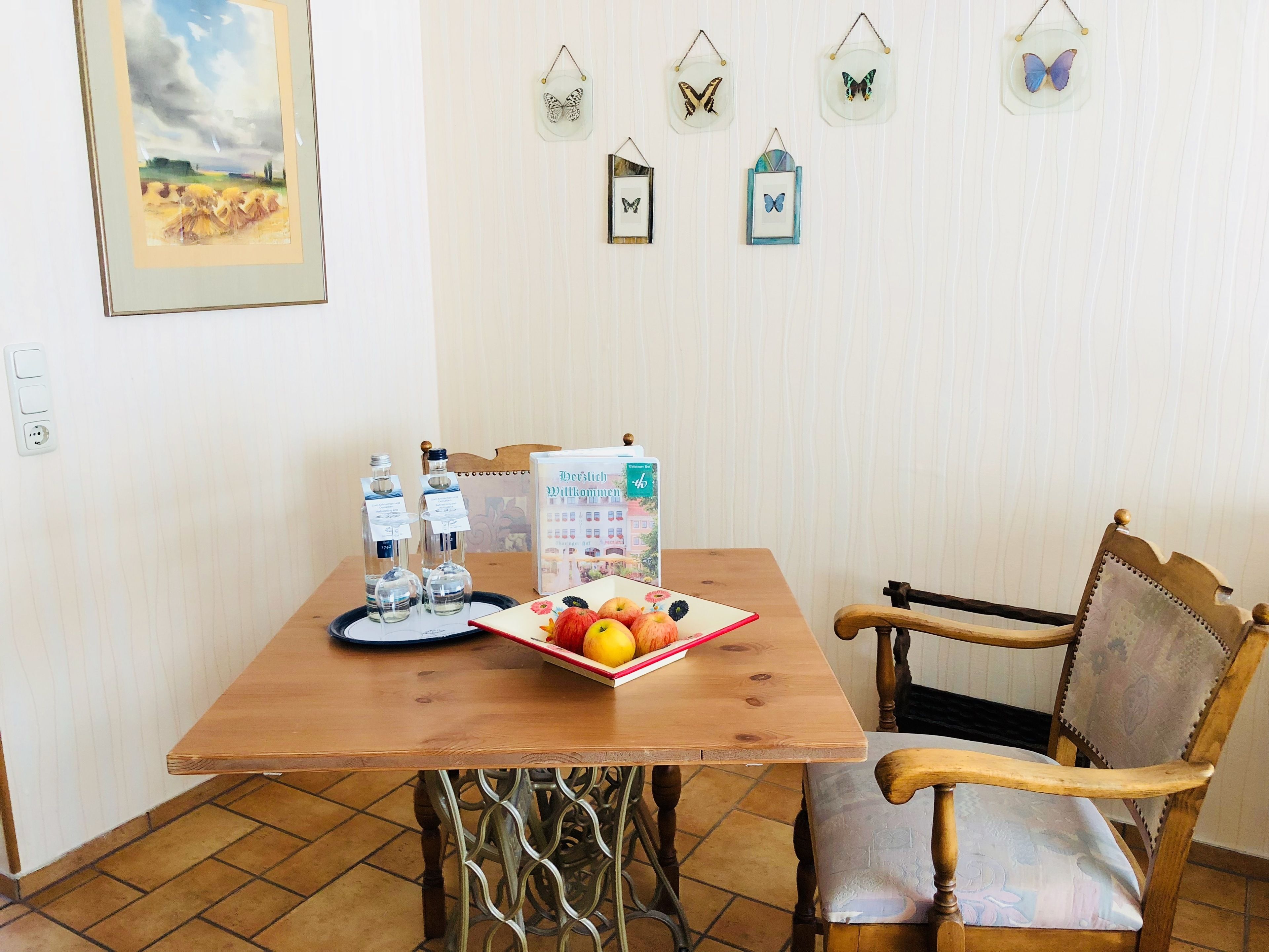 A wooden dining table with a fruit plate, two bottles, and a calendar. A chair is positioned to the right.