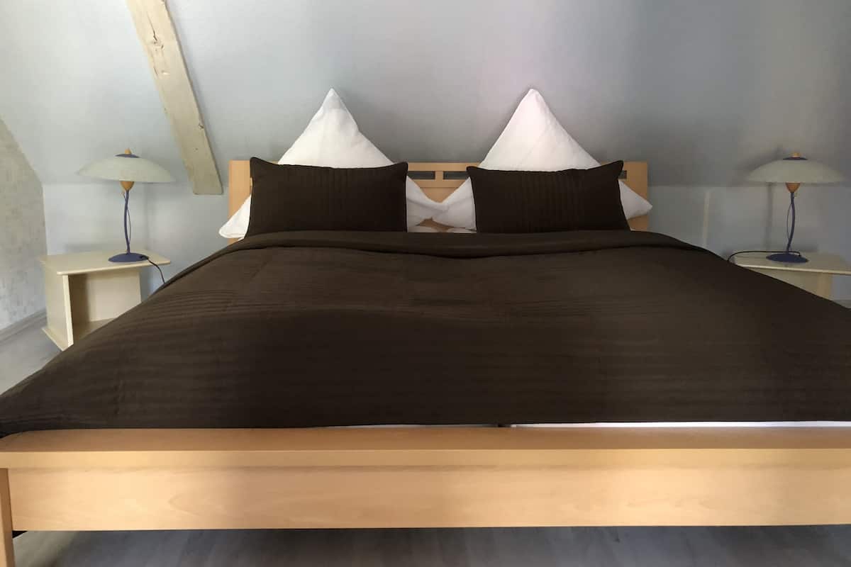 Una cama con cabecera de madera, dos mesitas de noche y dos lámparas.