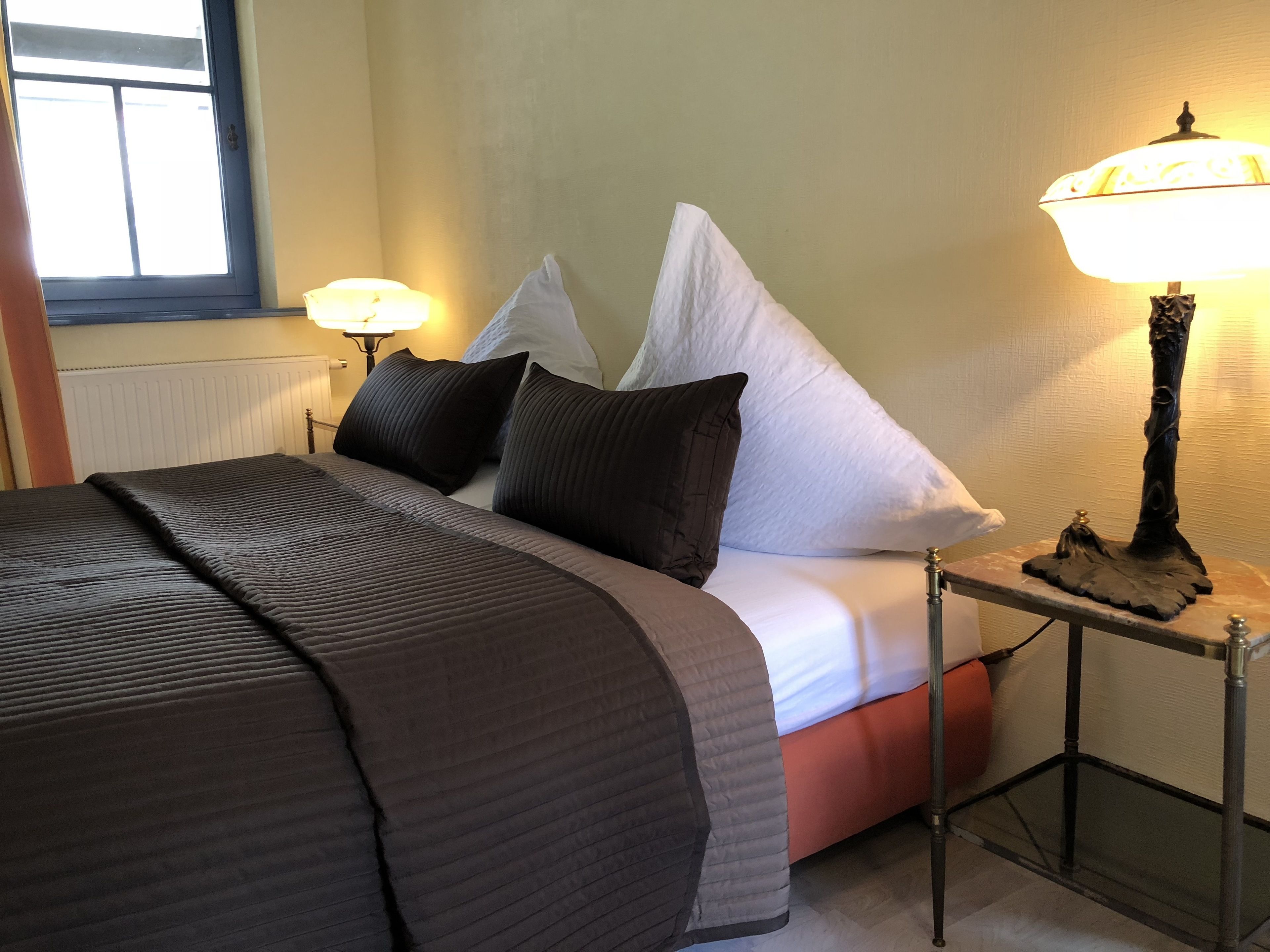 A neatly made bed with a dark brown quilt, white pillows, and a small table with a lamp beside it.