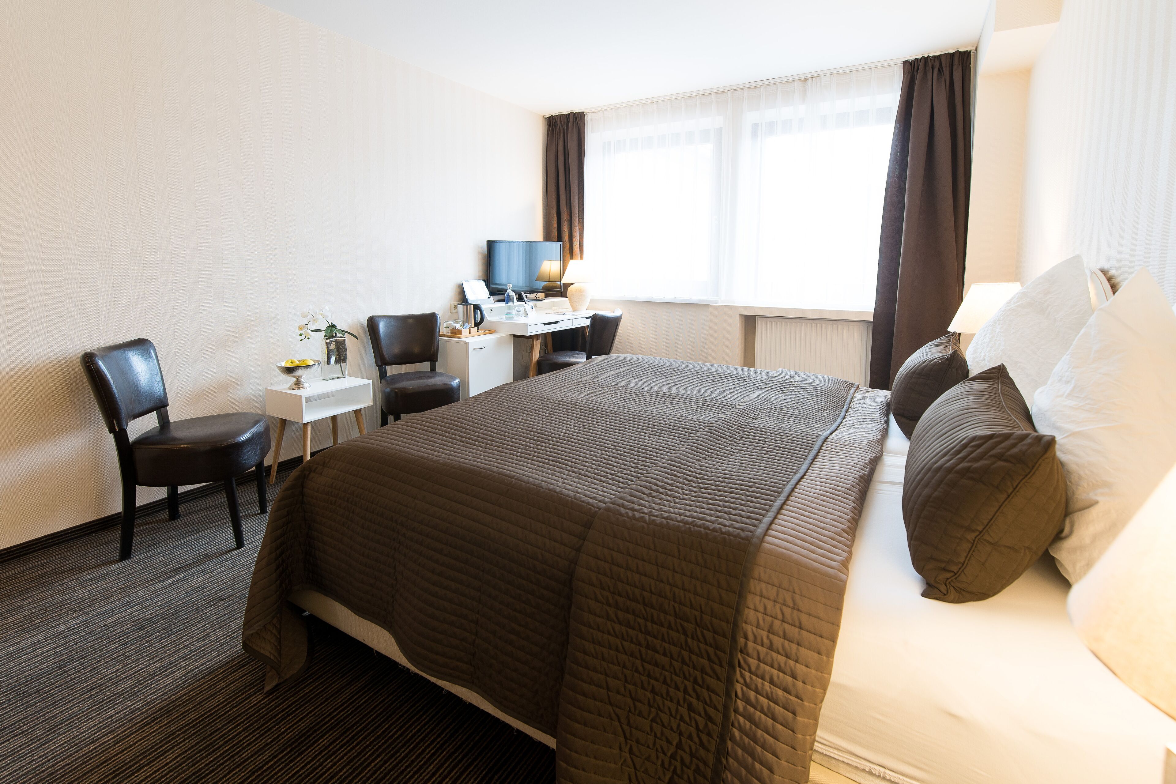 Ein Hotelzimmer mit einem großen Bett, einem Schreibtisch, einem Sessel und einem Fernseher.