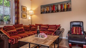Een gezellige woonkamer met een houten salontafel, een bank met gestreepte kussens, een leren fauteuil en een schilderij van kleurrijke boten aan de muur.