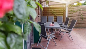 Een terras buiten met een tafel en stoelen, een houten hek en een bakstenen muur.