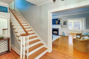 A staircase with wooden steps and white railings, leading to a room with a fireplace, wicker furniture, and a view of the outdoors. - Corpus Christi Home w/ Pool & Hot Tub: Walk to Bay (Corpus Christi)