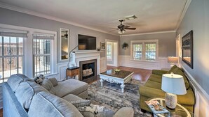 A living room with a fireplace, a ceiling fan, and a large window. - Corpus Christi Home w/ Pool & Hot Tub: Walk to Bay (Corpus Christi)