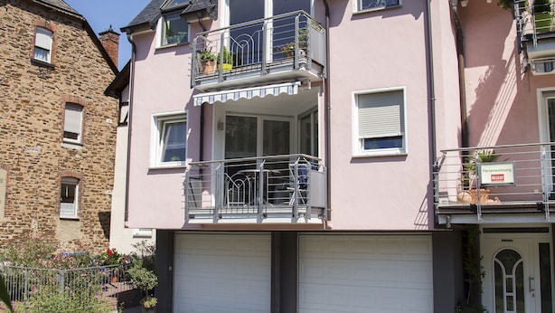Un edificio residenziale a due piani con garage, balconi e un vialetto in mattoni.