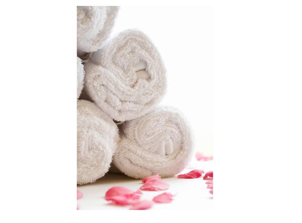 A stack of white towels with a rolled design, placed on a surface with scattered rose petals. - The Rhinos 6 (Guildford)