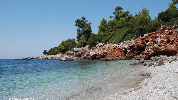 A beach with clear water, rocky terrain, and trees.