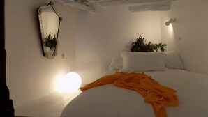 A bedroom with a bed, white walls, a mirror, and a bedside plant.