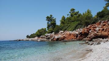 A beach with clear water, rocky terrain, and trees.