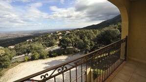Un balcon doté d’une balustrade en fer forgé, donnant sur une vallée parsemée d’arbres et de bâtiments.