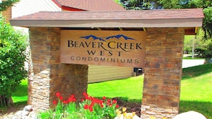 Une enseigne pour le complexe de condominiums Beaver Creek West, avec une structure en pierre et un espace verdoyant agrémenté de fleurs rouges.