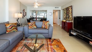 A living room with a sofa, coffee table, and TV. There is a kitchen in the background. - 2BR/2BA Remodeled-All Rooms are Oceanfront! 12th Floor-2 Balconies-Beach Locker! (Myrtle Beach)